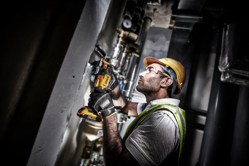 Arbeider gebruikt een DEWALT DCS355D2 gereedschap aan een muur, met veiligheidsuitrusting en handschoenen.
