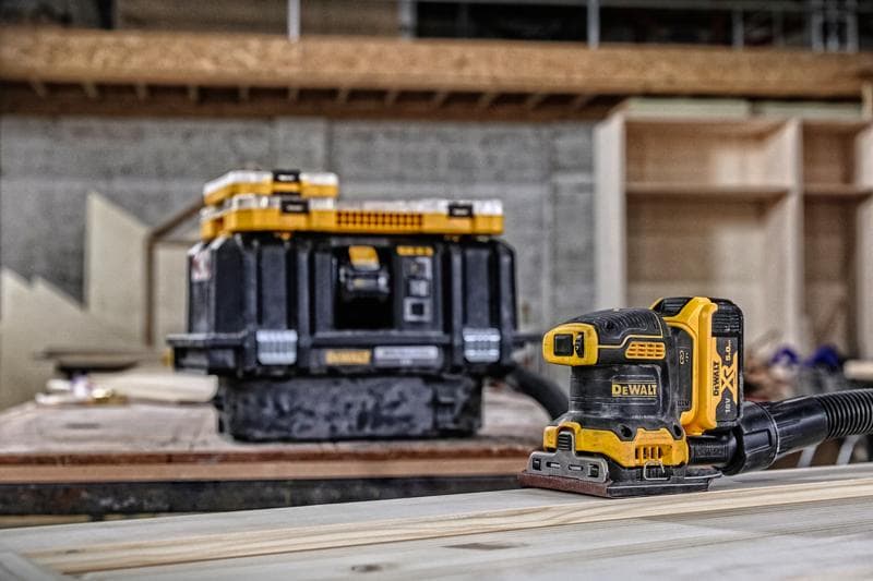 DEWALT draadloze schuurmachine op hout, opslagbox op de achtergrond in een werkplaats.