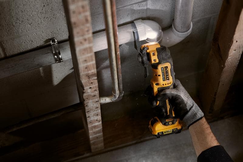 Persoon gebruikt een DEWALT snoerloos oscillerend gereedschap om een pijp bij een betonnen muur te snijden.