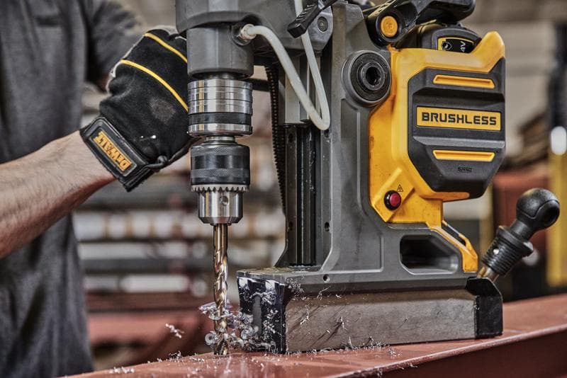 Persoon gebruikt DEWALT borstelloze magneetboormachine voor gatboren in metaal, met metaalspaanders op tafel.