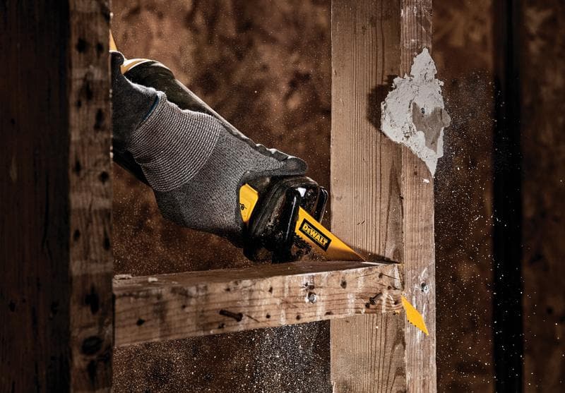 Close-up van een hand met een grijze handschoen die een DEWALT reciprozaag gebruikt om door een houten balk te zagen, terwijl zaagsel door de lucht vliegt.
