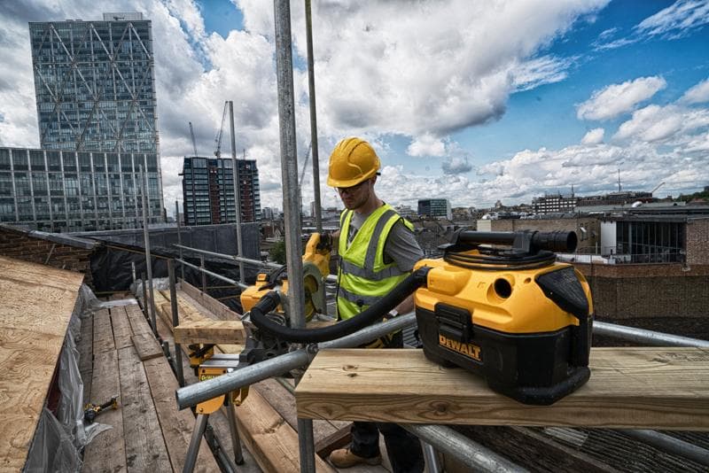 DEWALT DCV584-stofzuiger op een bouwplaats op het dak met een arbeider en stadsgebouwen op de achtergrond.
