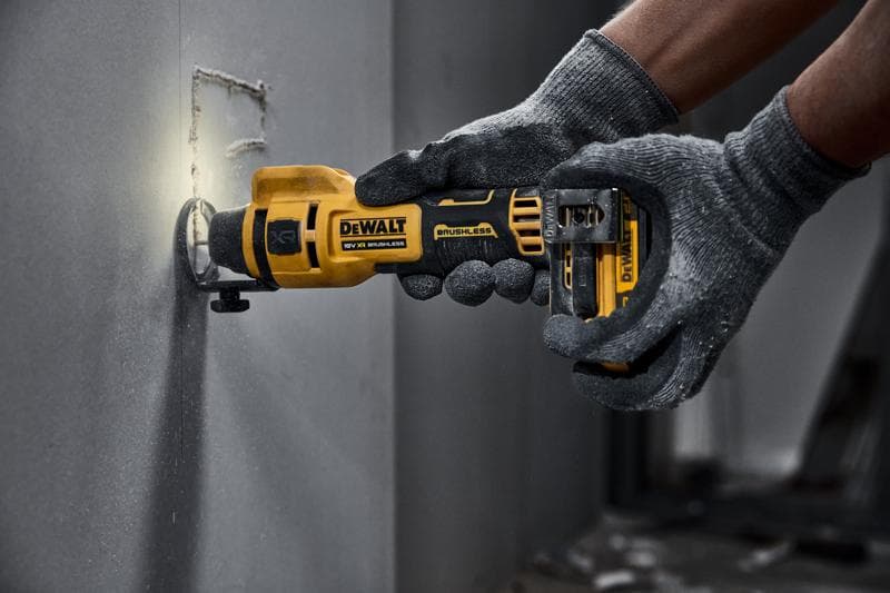 DEWALT draadloos roterend gereedschap snijdt in gipsplaat, bediend door gehandschoende handen.
