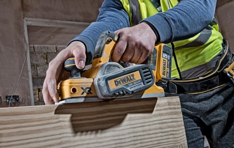 Persoon gebruikt een DEWALT DCP580N draadloze schaaf op hout bij een bouwplaats.