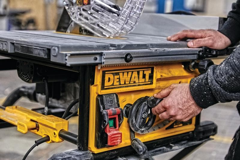 Close-up of a person adjusting the settings on a DEWALT table saw, featuring a yellow control panel with switches and dials in a workshop setting.