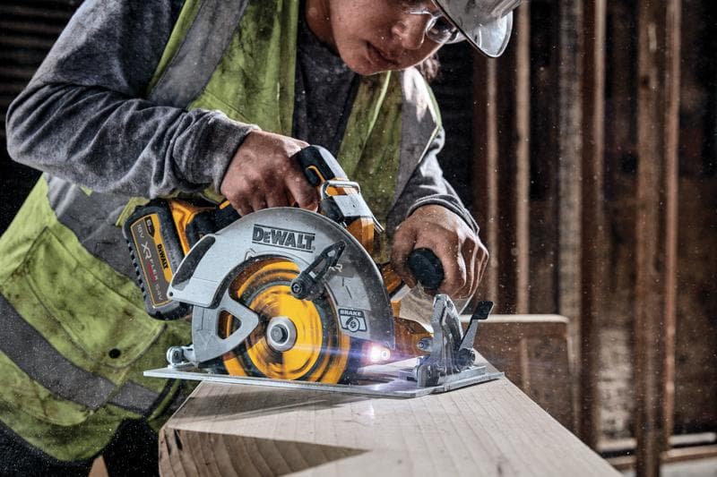 DEWALT draadloze cirkelzaag zaagt hout, gebruikt door een werker met vest op een bouwplaats.
