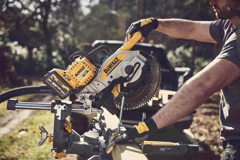 Iemand zaagt hout buiten met een DEWALT draadloze verstekzaag; geel-zwarte tool met XR FLEXVOLT batterij.