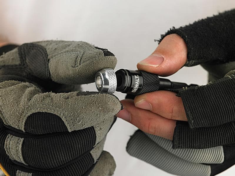 Hands met handschoenen houden een DEWALT bitshouder vast.