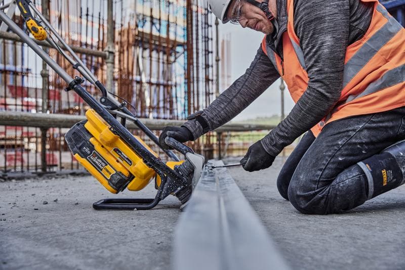 Werker zaagt met gele DEWALT gereedschap metaal op bouwplaats, draagt veiligheidskleding en oranje vest.