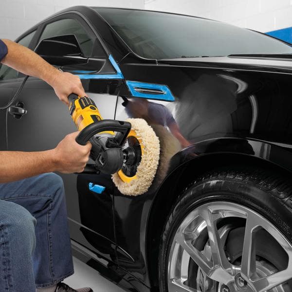 Persoon poetst een zwarte auto met een DEWALT polisher in een garage.