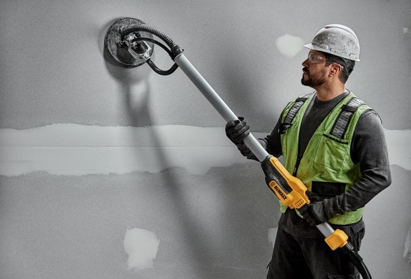 Werker gebruikt DEWALT DWE7800, DWE7800-QS wandschuurmachine op gipswand. Fotografieproduct.
