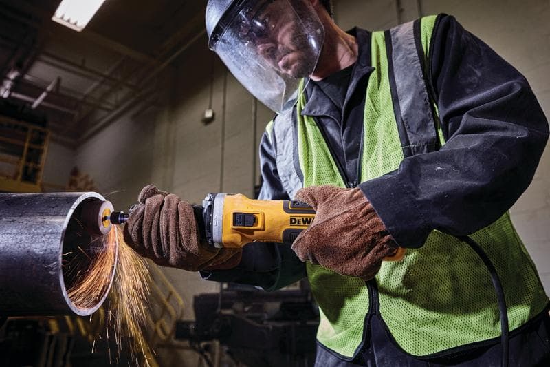Werker gebruikt DEWALT slijpmachine op metalen pijp, vonken vliegen, handschoenen en veiligheidsgordel binnen.