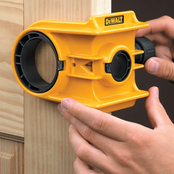 Een persoon gebruikt een geel DEWALT deurcilinderslot installatiekit om een gat op een houten deurkozijn uit te lijnen en te markeren.