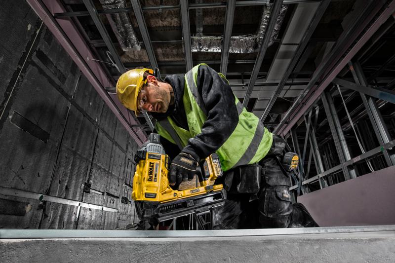 Werker met DEWALT DCN890P2 nagelapparaat, helm en veiligheidsvest op een bouwplaats.