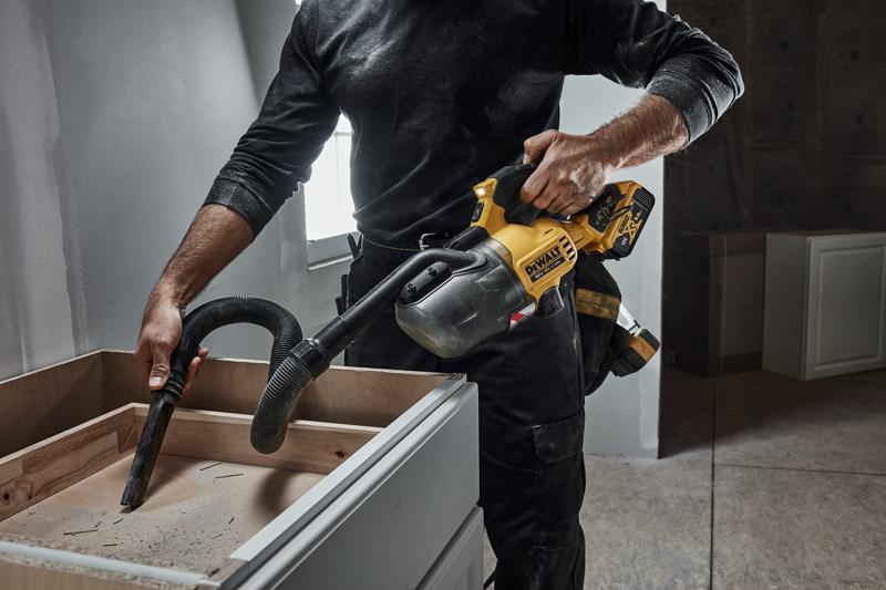 Persoon gebruikt een DEWALT draadloze handstofzuiger voor het reinigen van een houten kast tijdens renovatie.