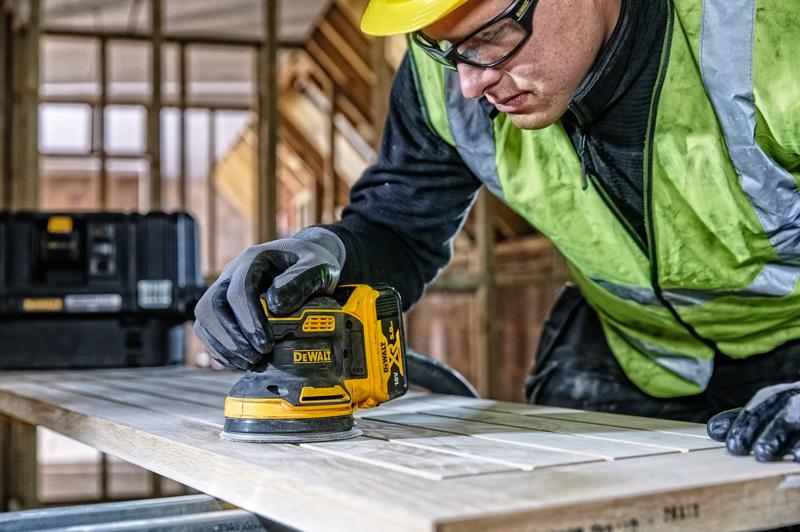 DEWALT DCW210, DCW210D1 schuurmachine gebruikt op hout, bouwlocatie, persoon draagt handschoenen en veiligheidsvest.