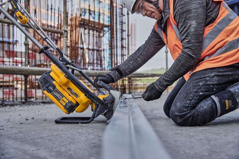 Werker zaagt met gele DEWALT gereedschap metaal op bouwplaats, draagt veiligheidskleding en oranje vest.