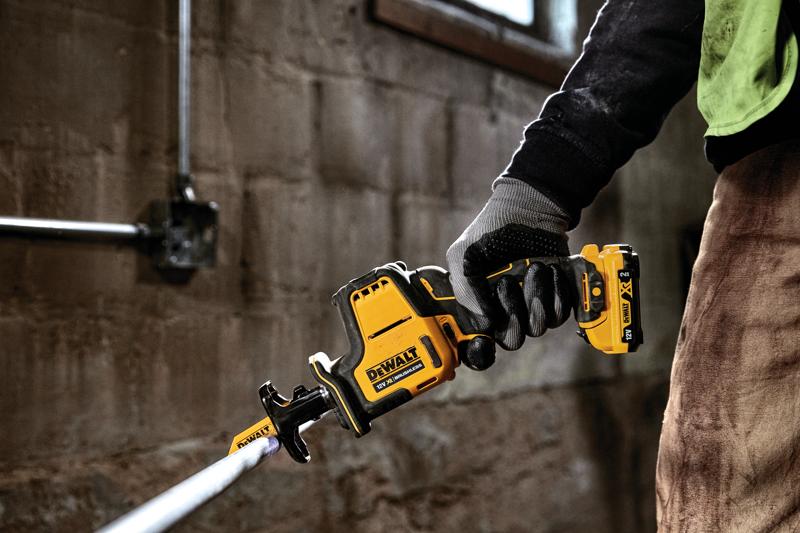 Een gehandschoende hand gebruikt een DEWALT snoerloze reciprozaag om een buis door te zagen.