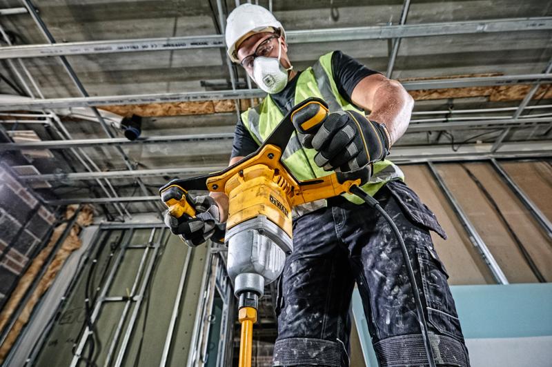 Persoon gebruikt DEWALT DWD241 mixerboor op bouwplaats, met veiligheidsuitrusting en handschoenen.